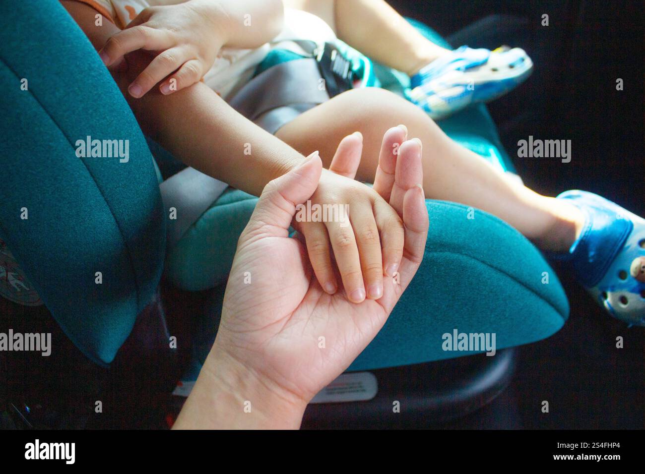 Mutter und Baby sitzen im Auto, Baby Hand in Mutter Hand, Kind sitzt auf einem sicheren Autositz Stockfoto