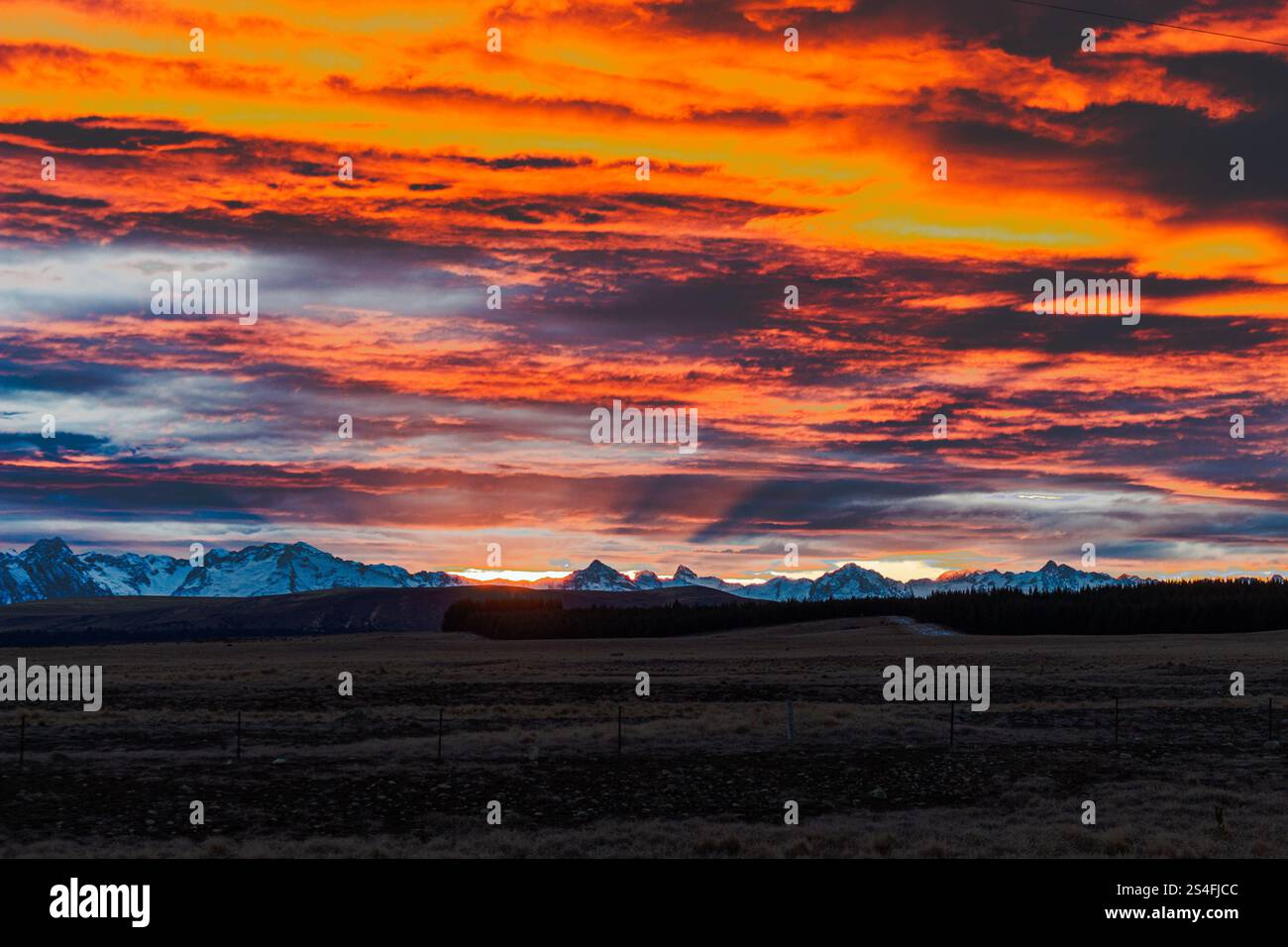 Alpine Sonnenuntergang, Rot- und Orangetöne über schneebedeckten Bergen und einer ruhigen ländlichen Landschaft, Südinsel, Neuseeland Stockfoto