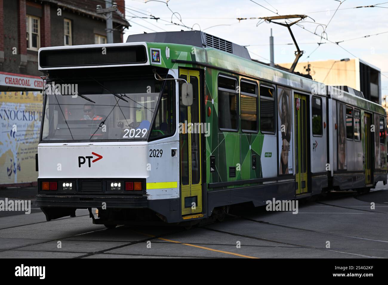 Straßenbahn der B-Klasse mit weißer und grüner Lackierung und PTV-Logo auf der Vorderseite, die abends eine Kreuzung im Vorort Melbourne überquert Stockfoto