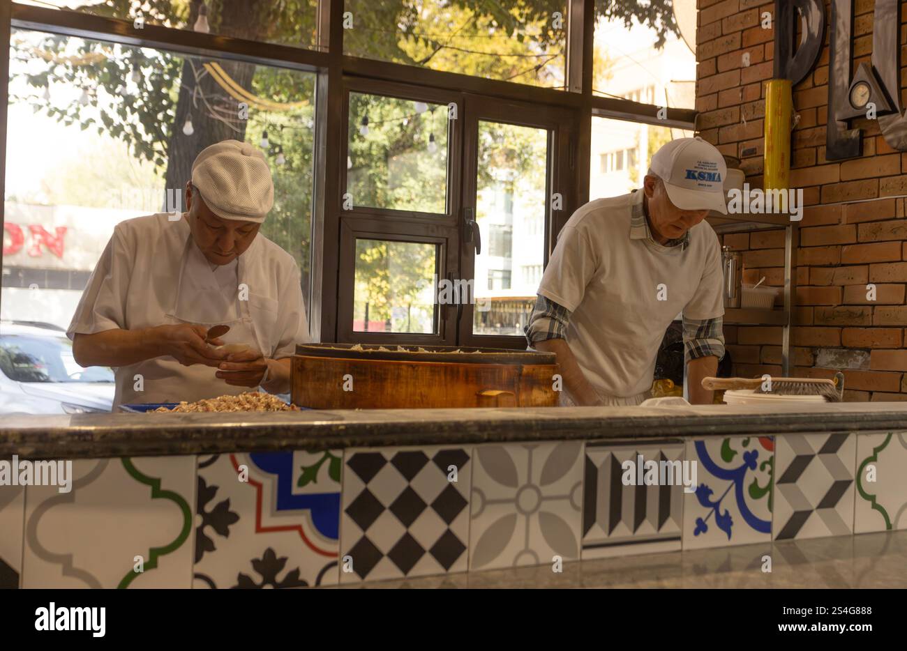 Bischkek, Kirgisistan - 11. Oktober 2024: Zwei Köche bereiten das Manti in offener Küche zu. Manti ist eine Art Knödel, die hauptsächlich in der türkischen Küche und zu finden ist Stockfoto