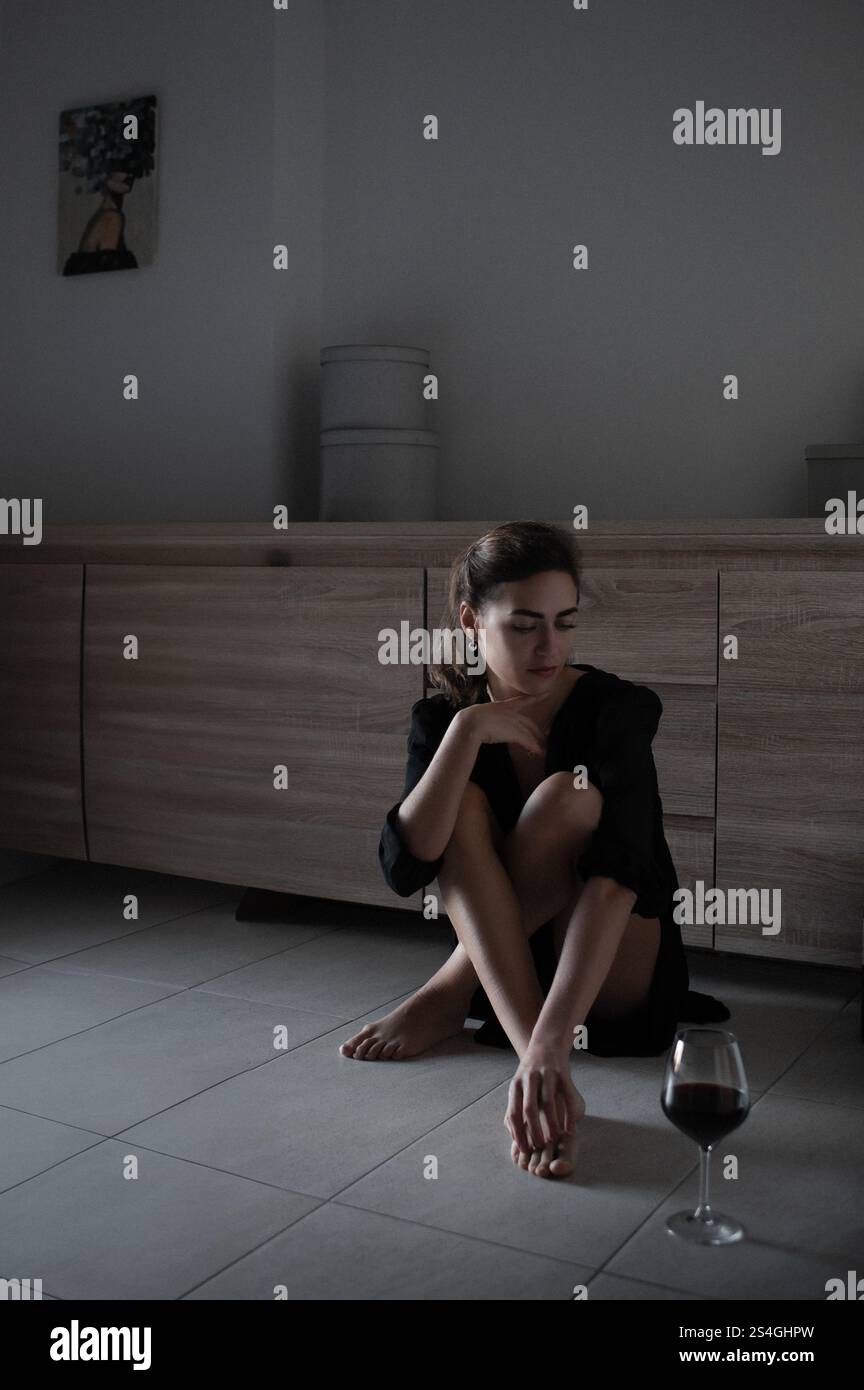 Frau in schwarzem Kleid entspannt sich zu Hause in gemütlicher Atmosphäre mit einem Glas Rotwein und einer Katze Stockfoto