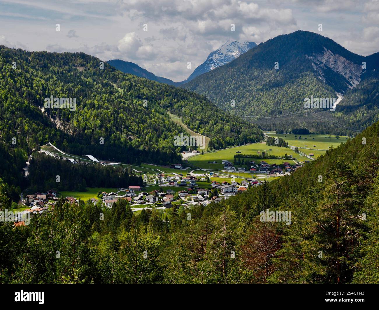 Malerisches Bergdorf umgeben von üppigen grünen Wäldern und schneebedeckten Gipfeln in den europäischen Alpen Stockfoto