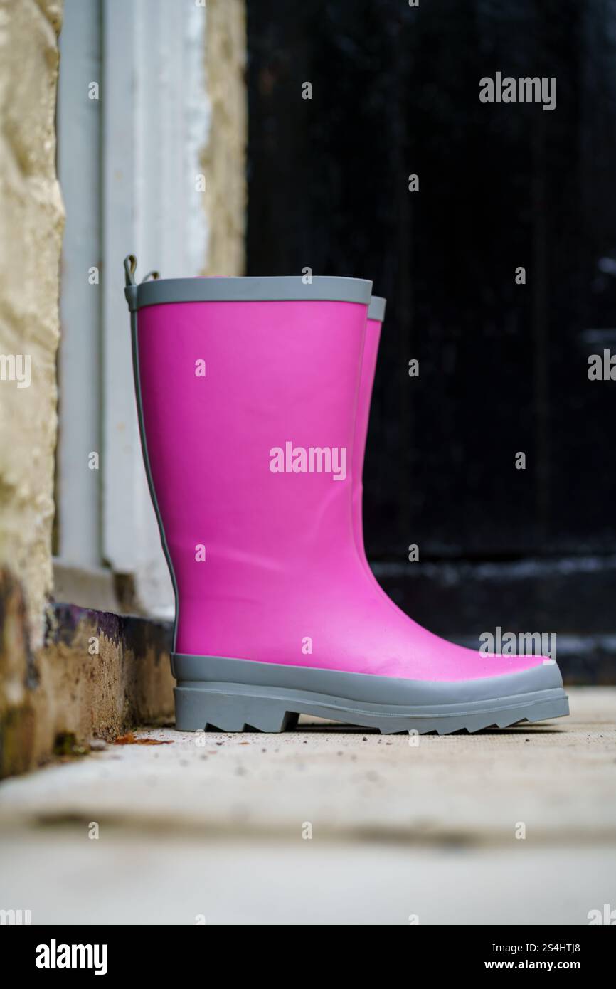 Ein leuchtend rosafarbener wellington-Gummistiefel steht aufrecht neben einer Steinmauer und steht im Kontrast zum gedämpften Hintergrund. Die lebendigen Farben des Schuhs und der Außenbereich Stockfoto