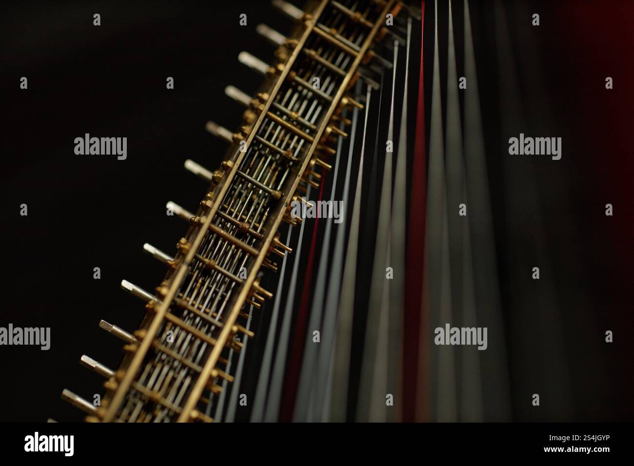 Nahaufnahme von spannenden Metallsaiten auf Stimmnadeln der antiken Harfe, aufgenommen in dunklem Innenlicht vor schwarzem Hintergrund, Kopierraum Stockfoto