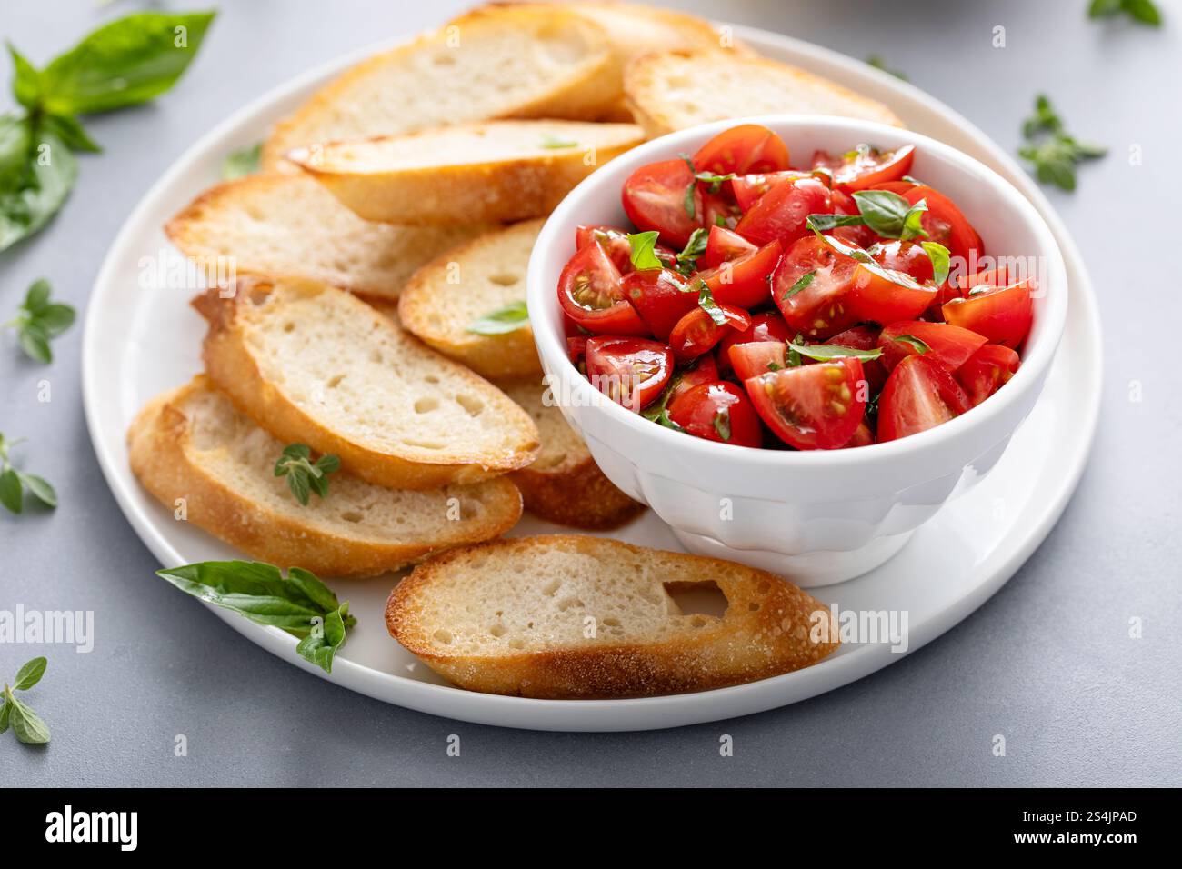 Reife Tomaten mit Basilikum in einer Schüssel neben geröstetem Baguette und Bruschetta Stockfoto