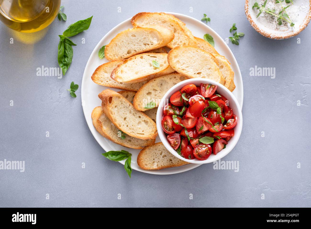 Reife Tomaten mit Basilikum in einer Schüssel neben geröstetem Baguette und Bruschetta Stockfoto