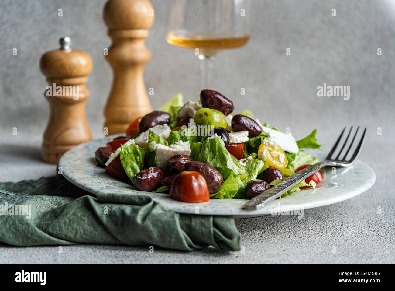 Ein lebhafter griechischer Salat mit Tomaten, Salat, roten Oliven, Fetakäse und Olivenöl Ein Glas kaltem Weißwein ergänzt die gesunde Mahlzeit Stockfoto