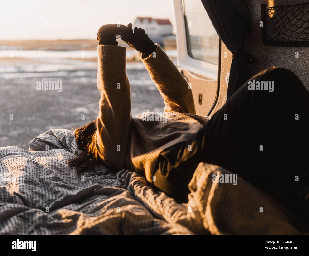 Nicht erkennbare Frau, die während eines Campingausflugs in Island in einem Van liegt. Sie streckt ihre Arme gegen das Sonnenlicht und schafft eine gemütliche, warme Atmosphäre Stockfoto Nicht erkennbare Frau, die während eines Campingausflugs in Island in einem Van liegt. Sie streckt ihre Arme gegen das Sonnenlicht und schafft eine gemütliche, warme Atmosphäre Stockfoto