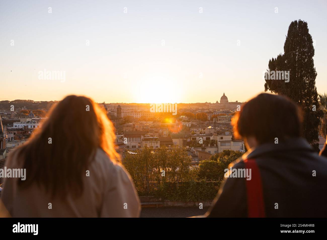 Ein atemberaubender Sonnenuntergang strahlt die berühmte Skyline Roms mit einem warmen Leuchten aus, während die Menschen den Blick bewundern. Die Szene verkörpert die reiche Geschichte der Stadt und die vibra Stockfoto