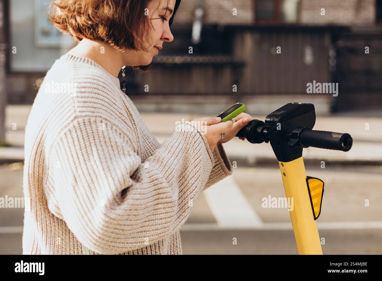 Eine Frau scannt mit ihrem Smartphone einen QR-Code, um einen Elektroroller zu mieten und steht an einem sonnigen Tag draußen. Die Szene fängt sie als ein Stockfoto