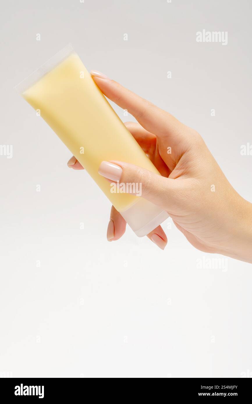 Eine Nahaufnahme einer zugeschnittenen, nicht erkennbaren Hand, die eine Tube gelbe Gesichtsmaske hält, die für Anti-Aging-Pflege mit Inhaltsstoffen wie m entwickelt wurde Stockfoto