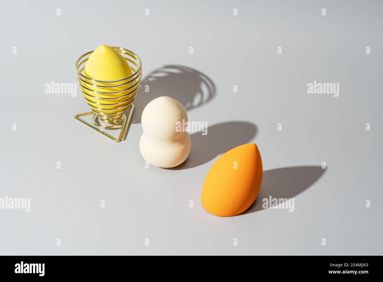 Eine Sammlung von bunten Kosmetikschwämmen, darunter ein gelber Schwamm in einem Metallhalter, ein weißer Schwamm und ein orangener Schwamm, angeordnet auf einem schlanken, Stockfoto