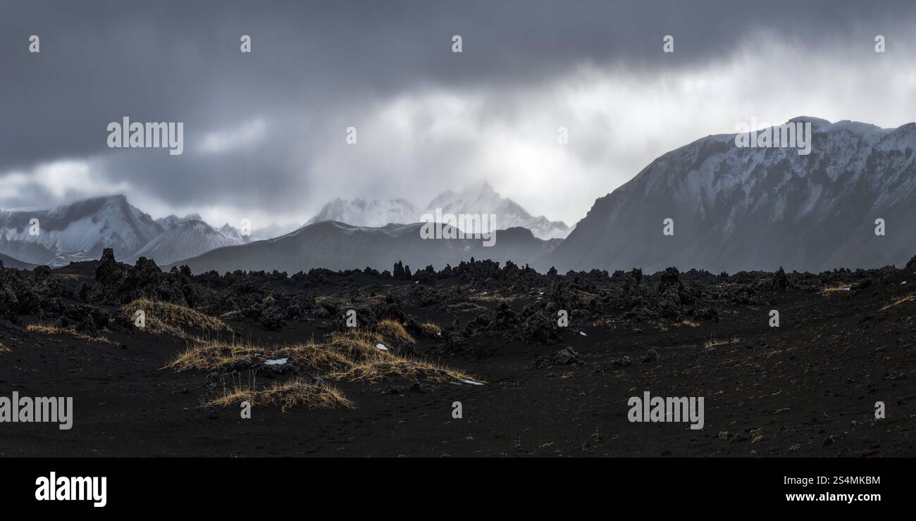 Majestätischer Panoramablick auf Islands Hochland mit vulkanischem Gelände und entfernten schneebedeckten Gipfeln unter einem stimmungsvollen, bewölkten Himmel strahlt die Szene eine wilde, Stockfoto