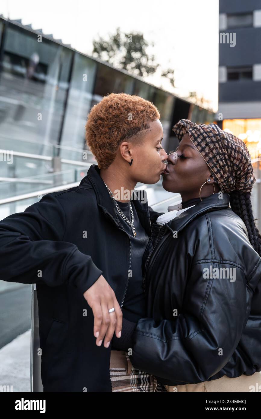 Ein liebevolles multiethnisches LGBT-Paar teilt sich einen zärtlichen Kuss in einer urbanen Umgebung. Sie sind stilvoll gekleidet und strahlen Wärme und Zuneigung aus. Die Szene Captu Stockfoto