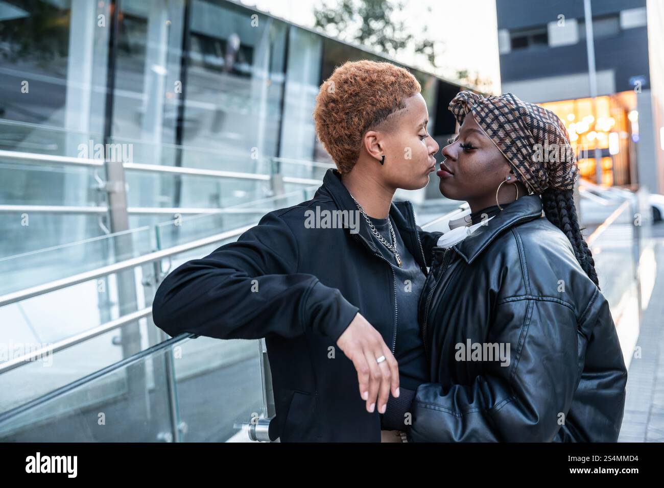 Ein zärtlicher Moment zwischen einem liebevollen, multiethnischen LGBT-Paar, das sich in einer urbanen Umgebung umgibt. Sie drücken Zuneigung aus, während sie sich umringt zu einem Kuss hineinlehnen Stockfoto