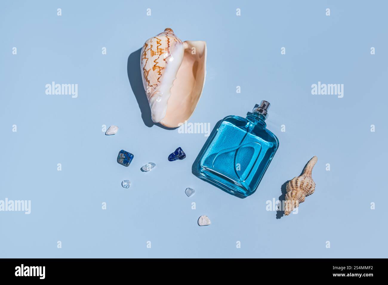 Eine blaue Parfümflasche, Muscheln und kleine Edelsteine sind kunstvoll auf einem sanften blauen Hintergrund angeordnet und erinnern an ein erfrischendes Küsten-Ambiente Stockfoto