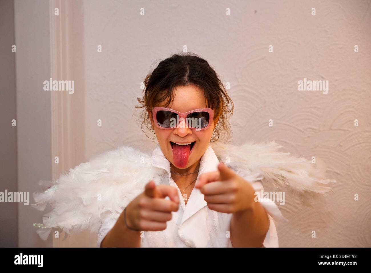 Junge Frau in weißem Outfit mit gefiederten Flügeln und Sonnenbrille Stockfoto