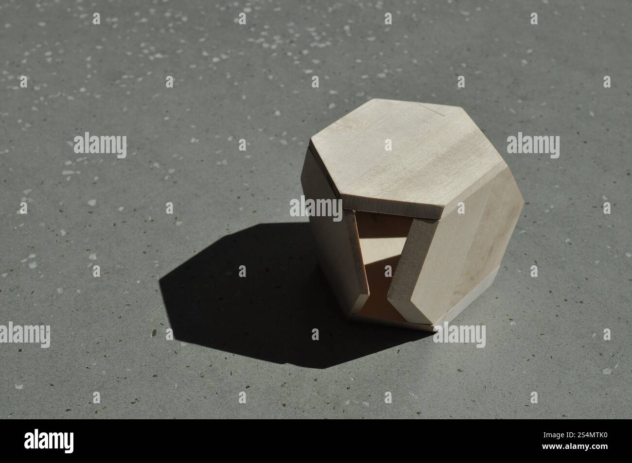 Ein sechseckiges Holzstück liegt auf einer Betonoberfläche und erzeugt einen Schatten Stockfoto