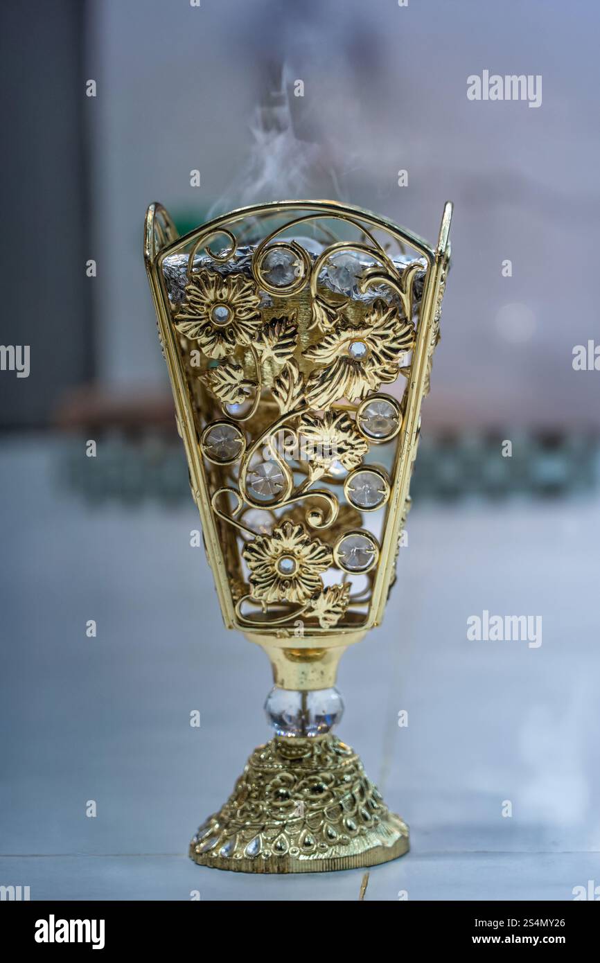 Ein wunderschön gestalteter goldener Omani Bakur-Topf mit komplizierten Blumenmustern strahlt sanften Rauch aus, der das kulturelle Erbe und traditionelle Werte repräsentiert Stockfoto
