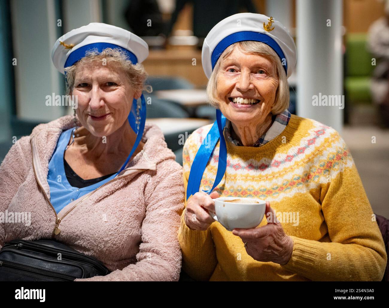 Troon, Schottland, Großbritannien. Januar 2025. Die viel verspätete und überteuerte Passagierfähre MV Glen Sannox macht ihre erste planmäßige Überfahrt zwischen Troon und Brodick auf der Isle of Arran. Die kaledonische MacBrayne-Fähre ist sieben Jahre zu spät und viele Millionen Pfund über dem Budget. PIC; zwei Damen aus Troon mit Matrosenhüten, die einen Tagesausflug nach arran machen. Iain Masterton/Alamy Live News Stockfoto