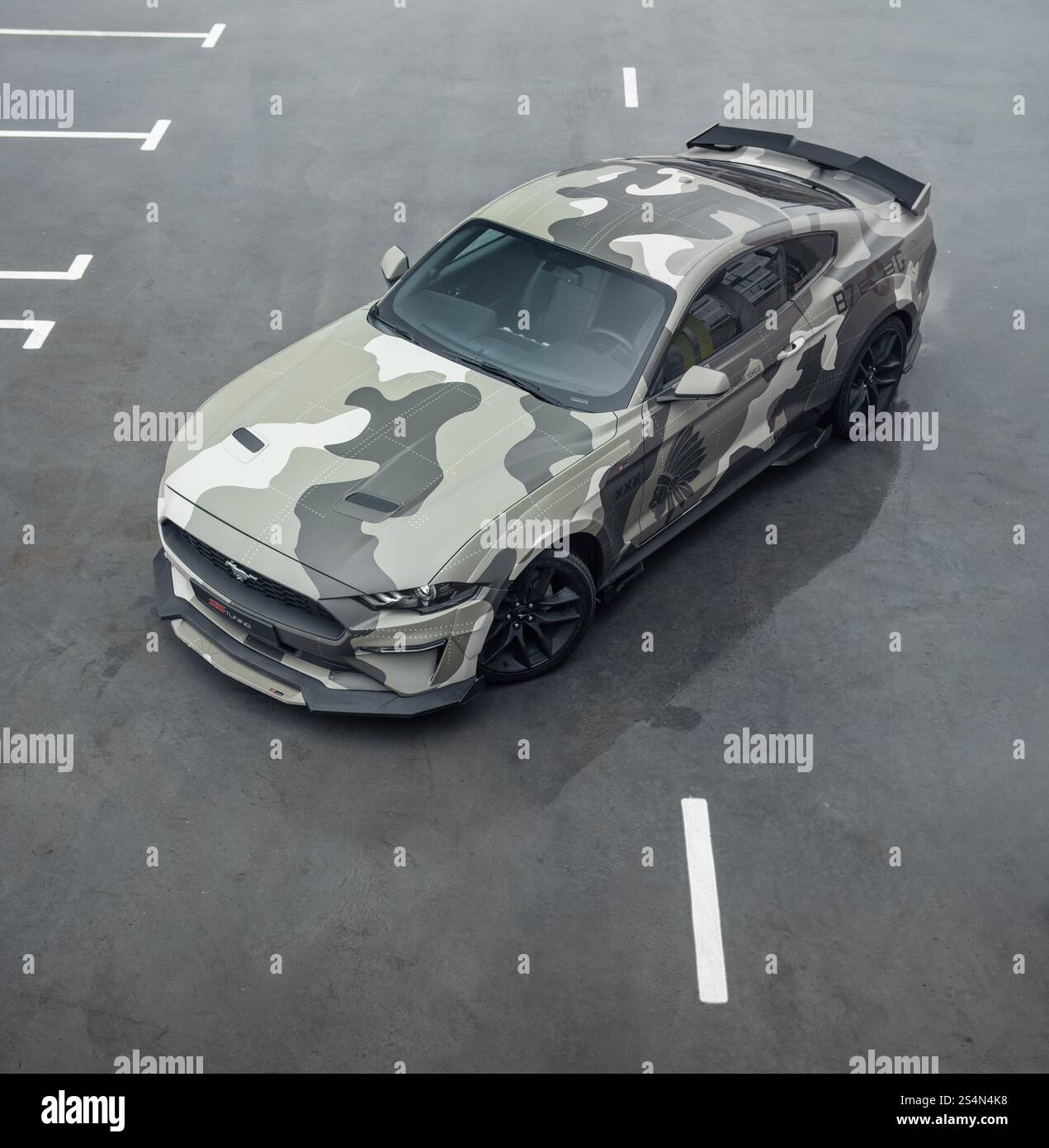 Grüner Camo Ford Mustang auf dem Parkplatz. Dreiviertelansicht eines amerikanischen Ponywagens, der auf nassem Betonboden geparkt ist. Stockfoto
