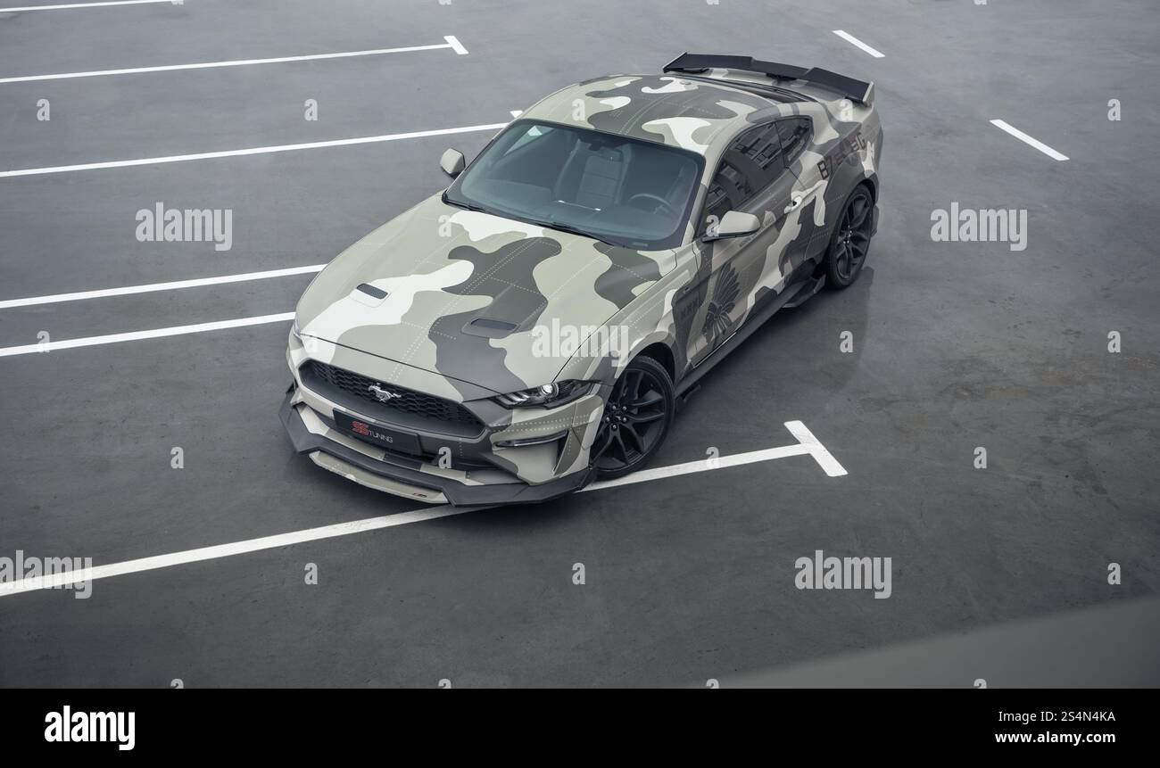 Grüner Camo Ford Mustang auf dem Parkplatz. Dreiviertelansicht eines amerikanischen Ponywagens, der auf nassem Betonboden geparkt ist. Stockfoto