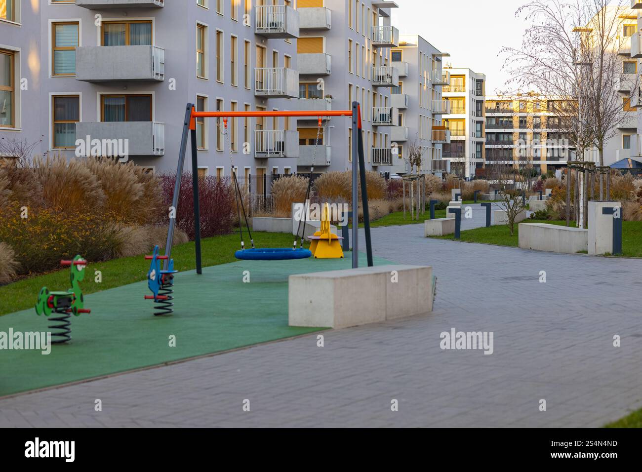 Moderner Innenhof mit Kinderspielplatz, umgeben von Apartmenthäusern und landschaftlich begrüntem Grün an einem sonnigen Abend Stockfoto