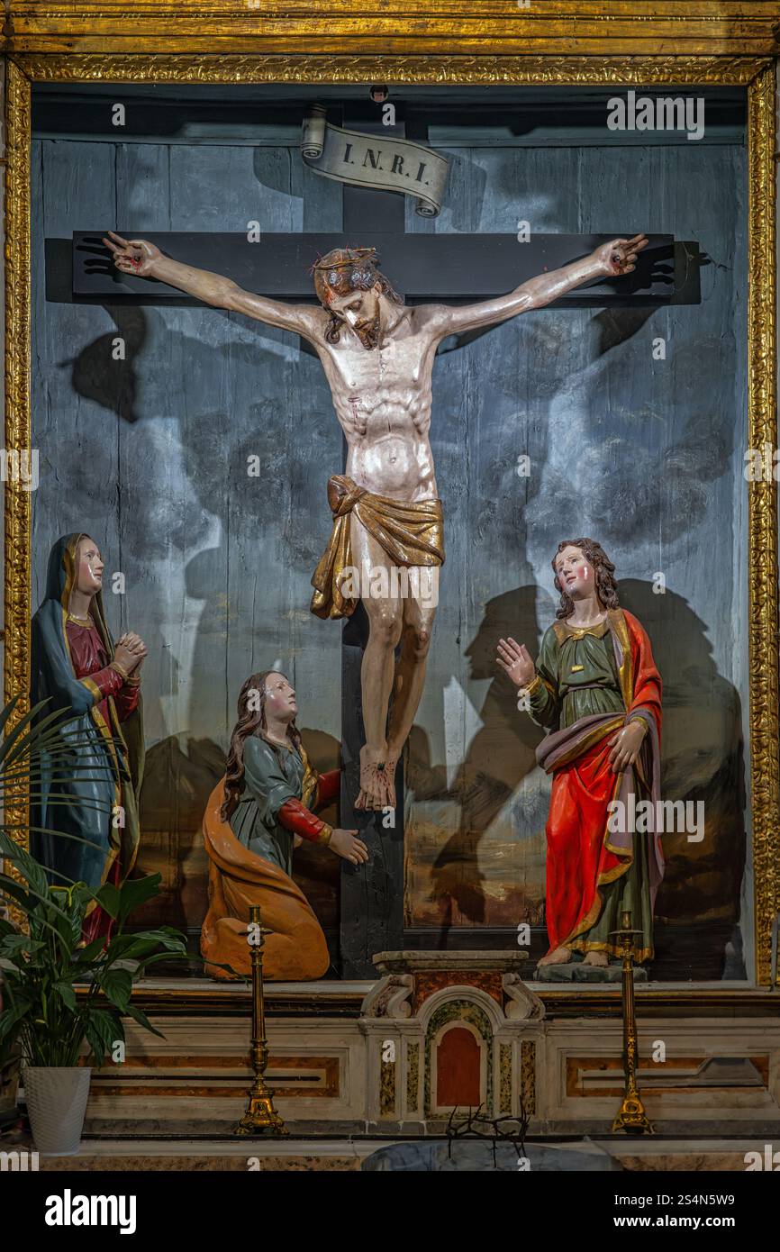 Hölzerne Statue von Jesus Christus am Kreuz mit der Jungfrau Maria und Maria Magdalena, die zu seinen Füßen in der Wallfahrtskirche der Himmelfahrt beten. Gu Stockfoto