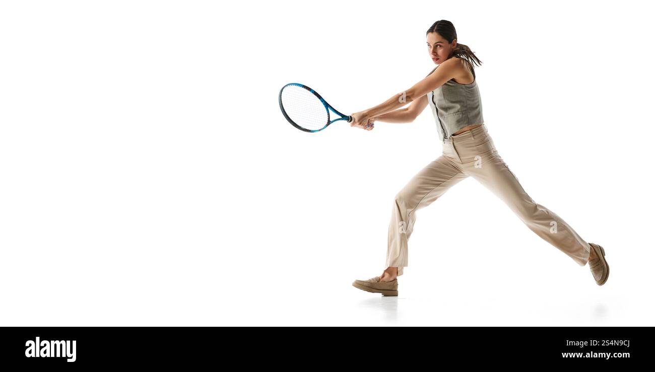 Frau in grauer Weste und beigefarbener Hose im Halbschwung mit Tennisschläger, symbolisiert Präzision und Effizienz bei der Umsetzung von Geschäftsstrategien gegen weiß Stockfoto