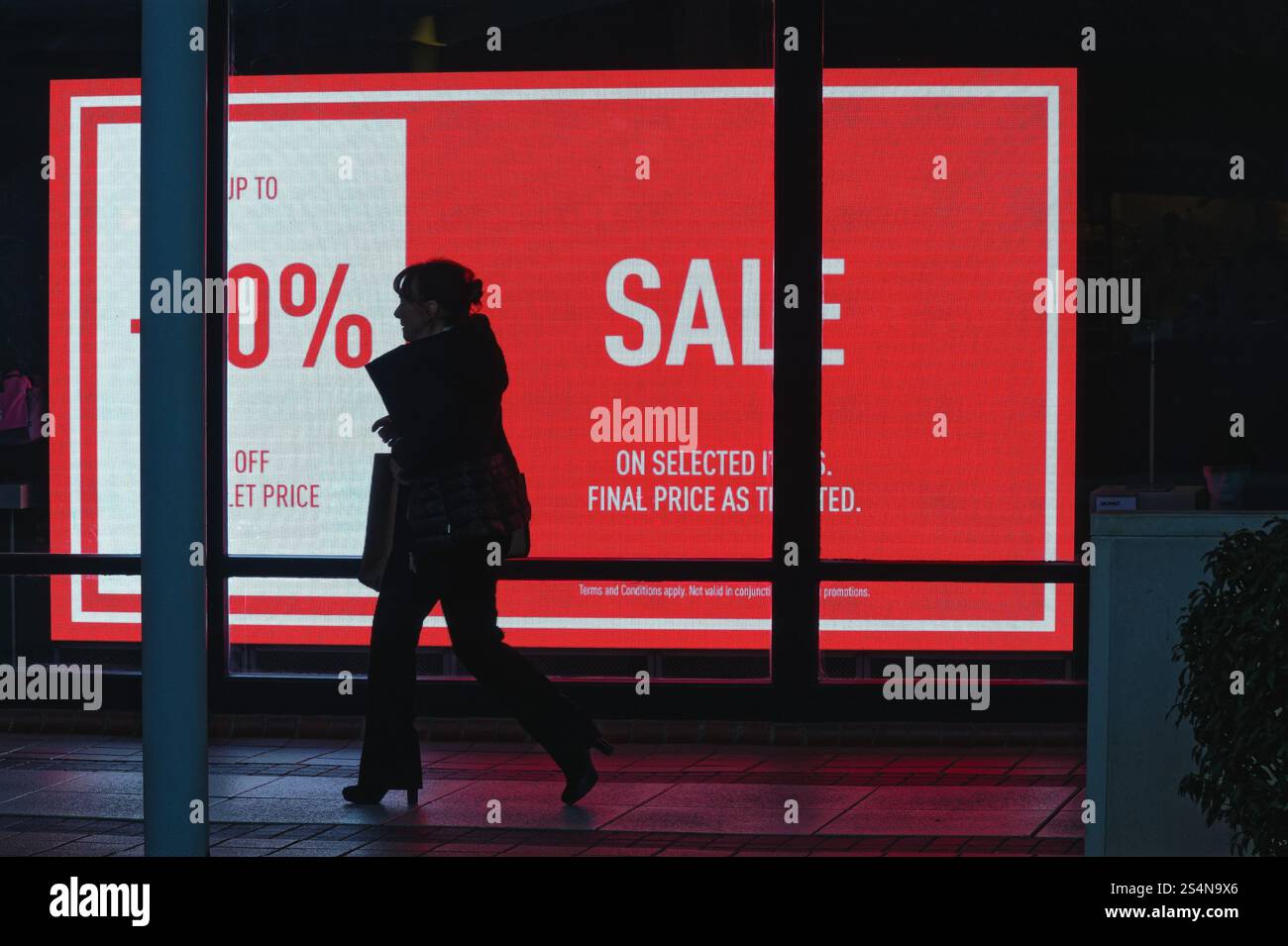 Silhouette einer Käuferin, die vor einem elektronischen Verkaufsschild in einem Schaufenster läuft, England UK Stockfoto