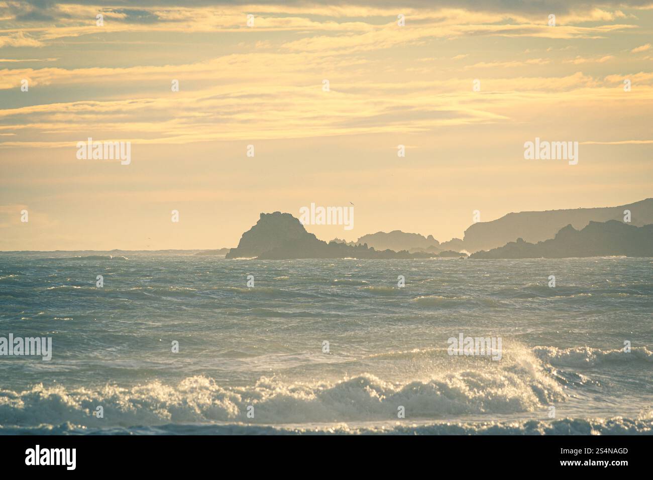 Wellen, die auf den Strand Rollen, blicken auf die Felsen Howe Loup, während die Sonne tief am Himmel ein goldenes Licht über Cruden Bay Beach in Aberdeens wirft Stockfoto