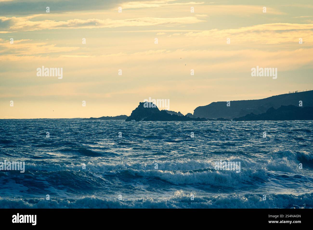 Wellen, die auf den Strand Rollen, blicken auf die Felsen Howe Loup, während die Sonne tief am Himmel ein goldenes Licht über Cruden Bay Beach in Aberdeens wirft Stockfoto