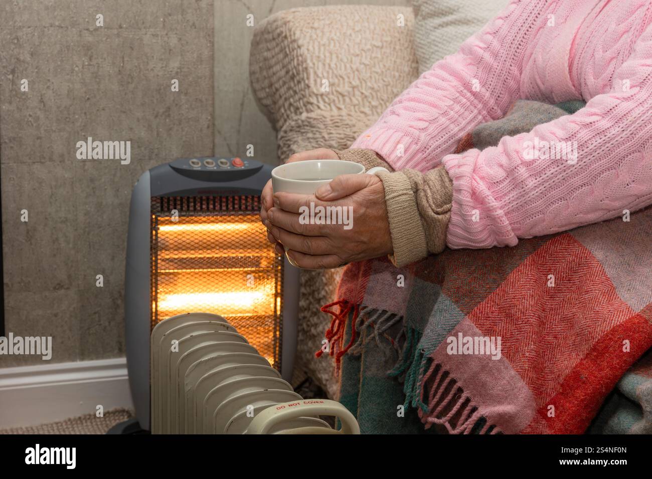 Rentnerin, die sich während der Kälte warm hält, Januar 2025 mit gekleideter Kleidung, Elektroheizgeräten und warmem Getränk. 2024 wurde die Labour G neu gewählt Stockfoto