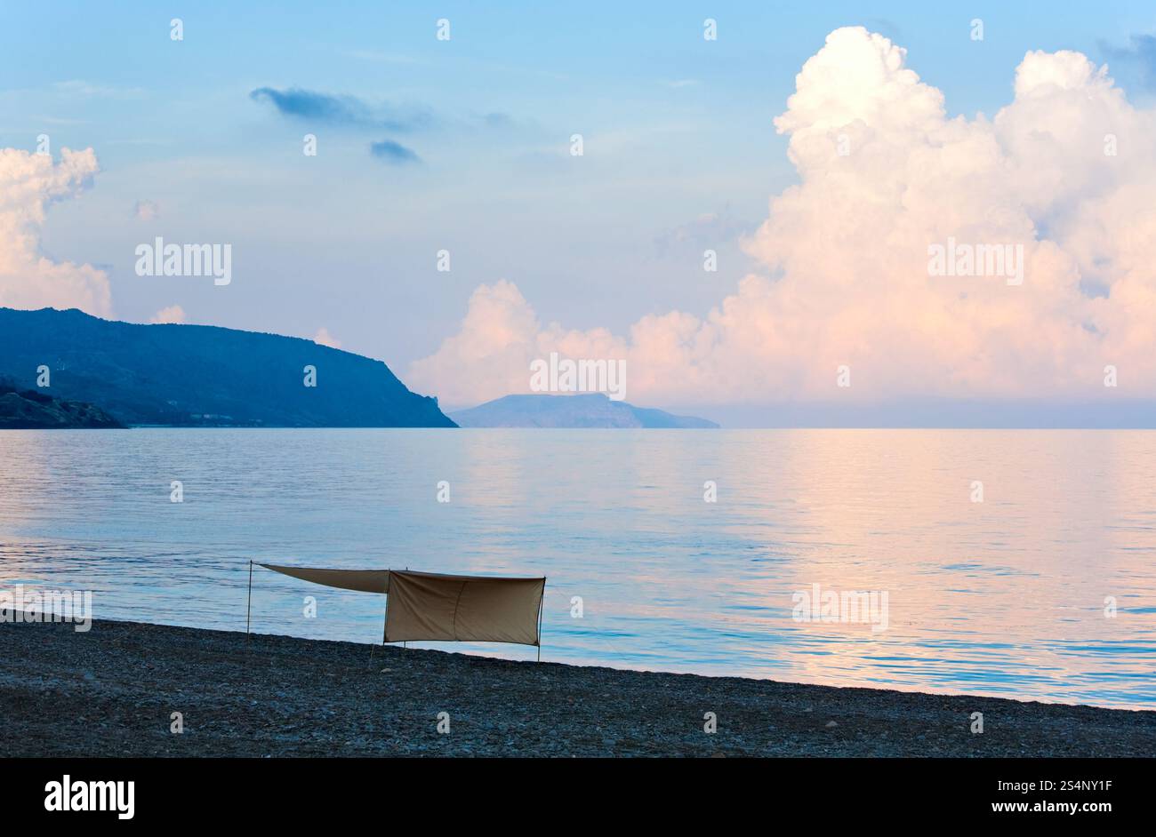 Sonnenuntergang in sanften rosa-blauen Farben, glänzende Oberfläche und Sonnenschirm am Strand (Krim, Ukraine). Stockfoto