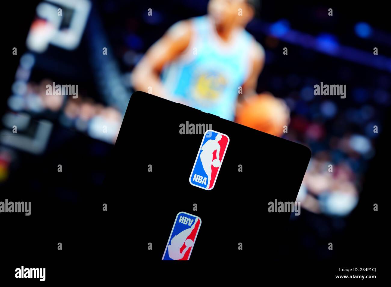 Ein Smartphone mit dem NBA-Logo und einem unscharfen Basketballspiel im Hintergrund. Januar 2025 Stockfoto