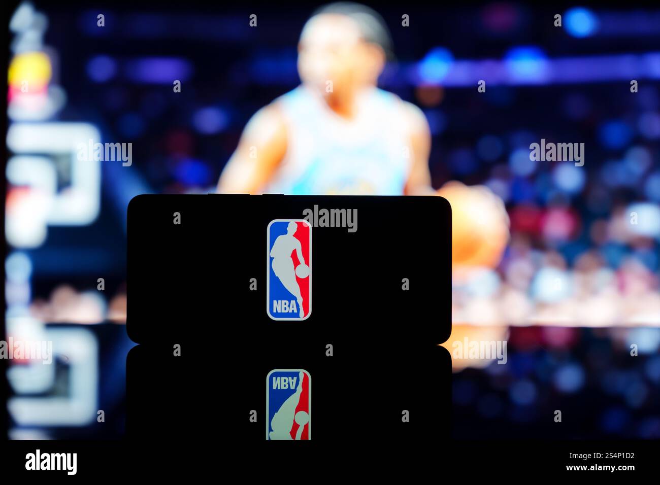 Ein Smartphone mit dem NBA-Logo und einem unscharfen Basketballspiel im Hintergrund. Januar 2025 Stockfoto