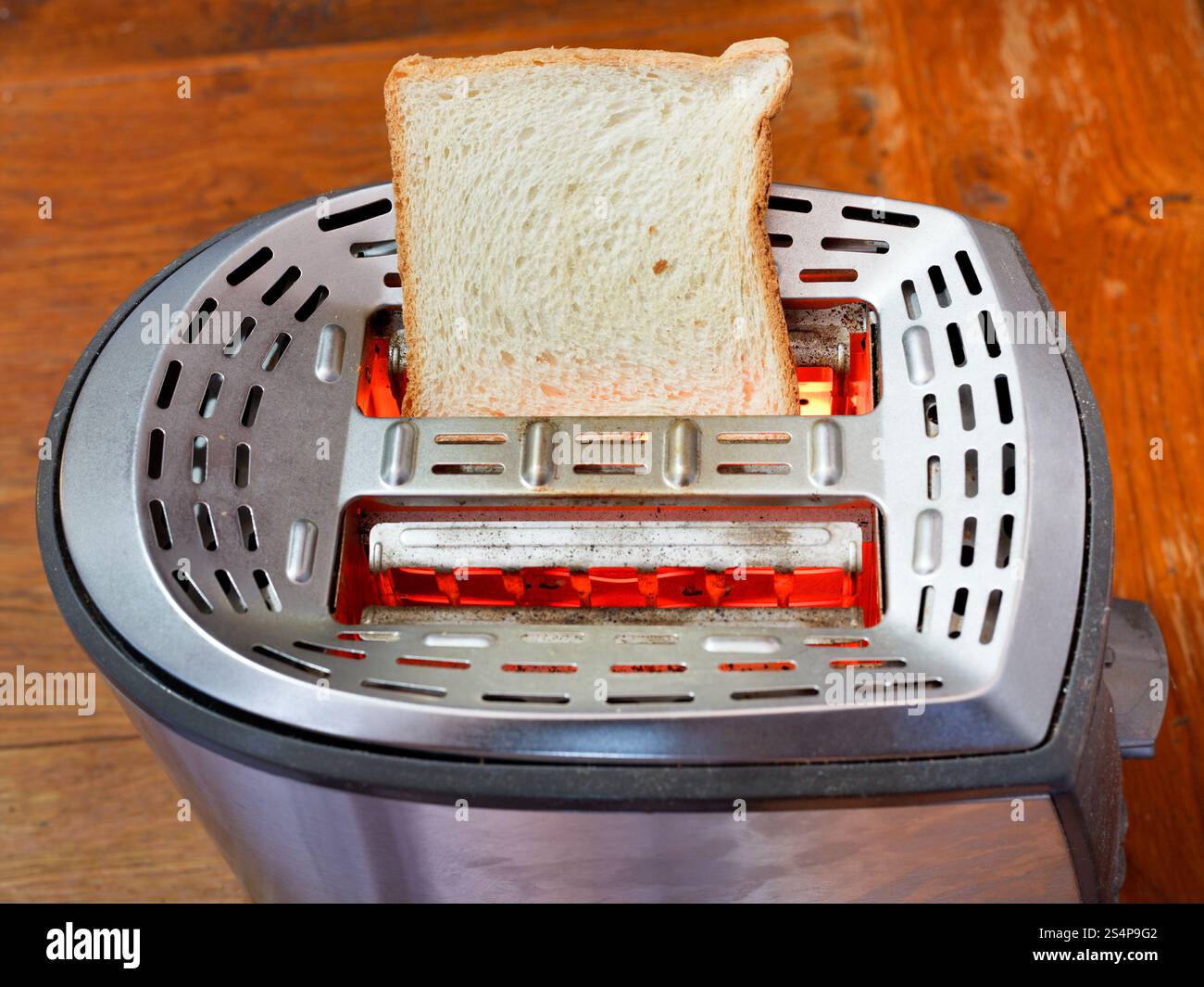 eine frische Scheibe Brot auf heißem Metall Toaster auf Holztisch Stockfoto