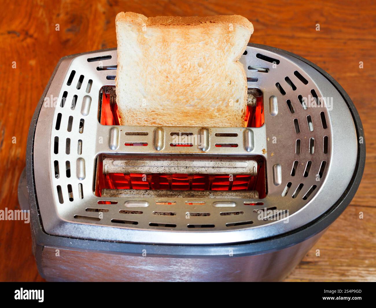 eine geröstete Brotscheibe auf heißem Metall Toaster auf Holztisch Stockfoto