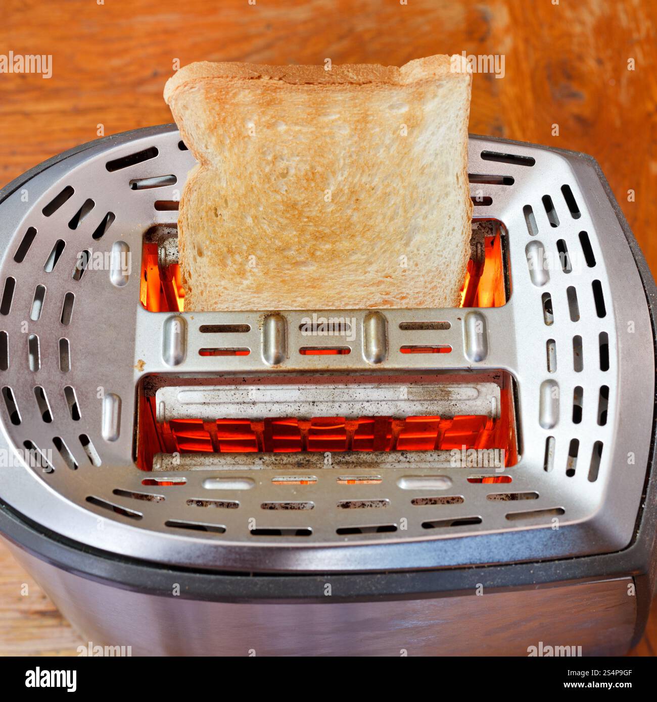 Gebackener Toast auf heißem Metalltoaster am Holztisch Stockfoto