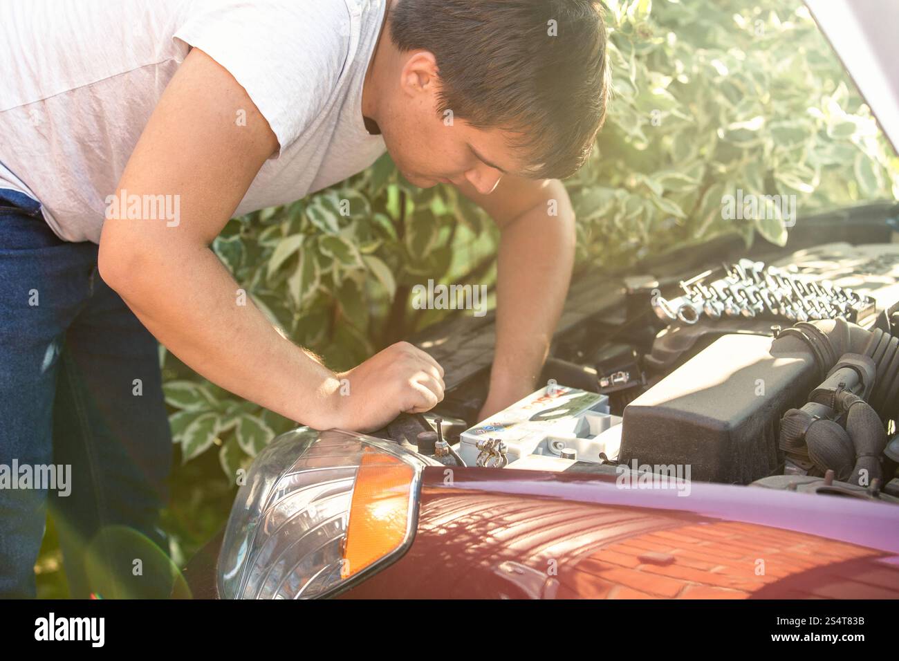 Junger Mann mit Blick auf offene Motorhaube und Motor reparieren Stockfoto