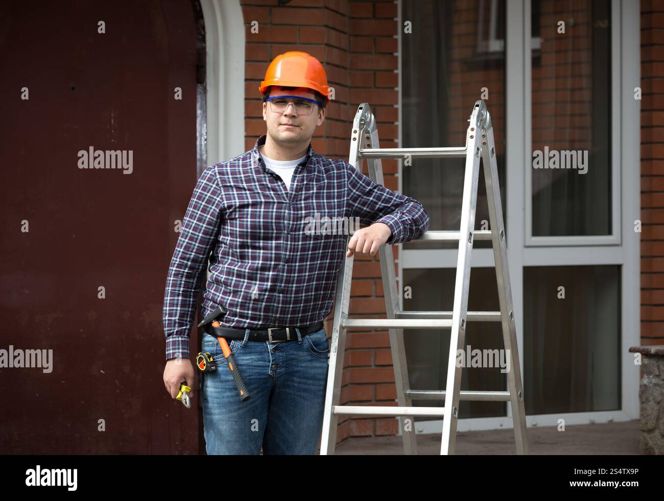 Porträt der lächelnde Arbeiter in Schutzhelm gelehnt Metallleiter Stockfoto