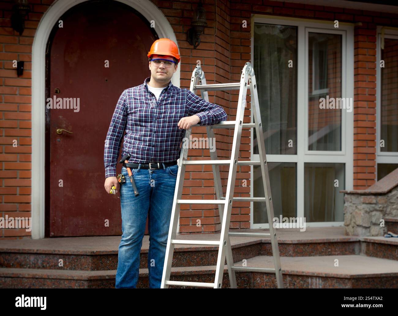 Berufsarbeitskraft posiert mit Metallleiter gegen Hausbau Stockfoto
