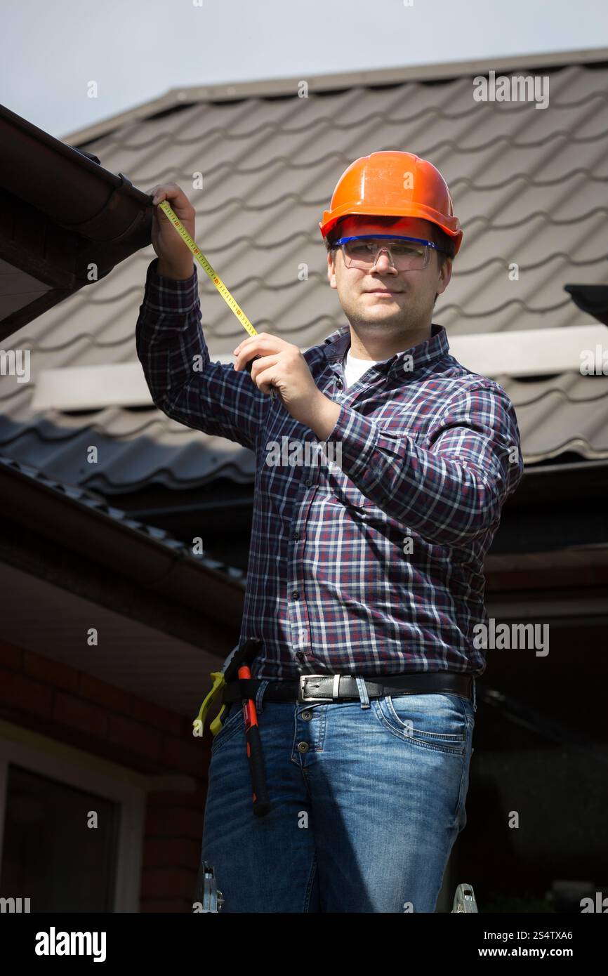 Junger Arbeiter in harten Hut, die Messung der Größe von Hausdach Stockfoto