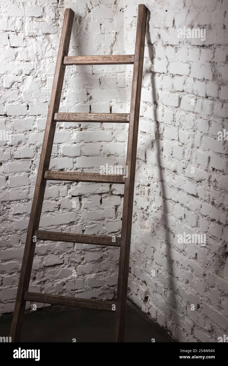 Studio-Foto einer alten Holzleiter, die an einer weißen Ziegelwand gelehnt ist Stockfoto