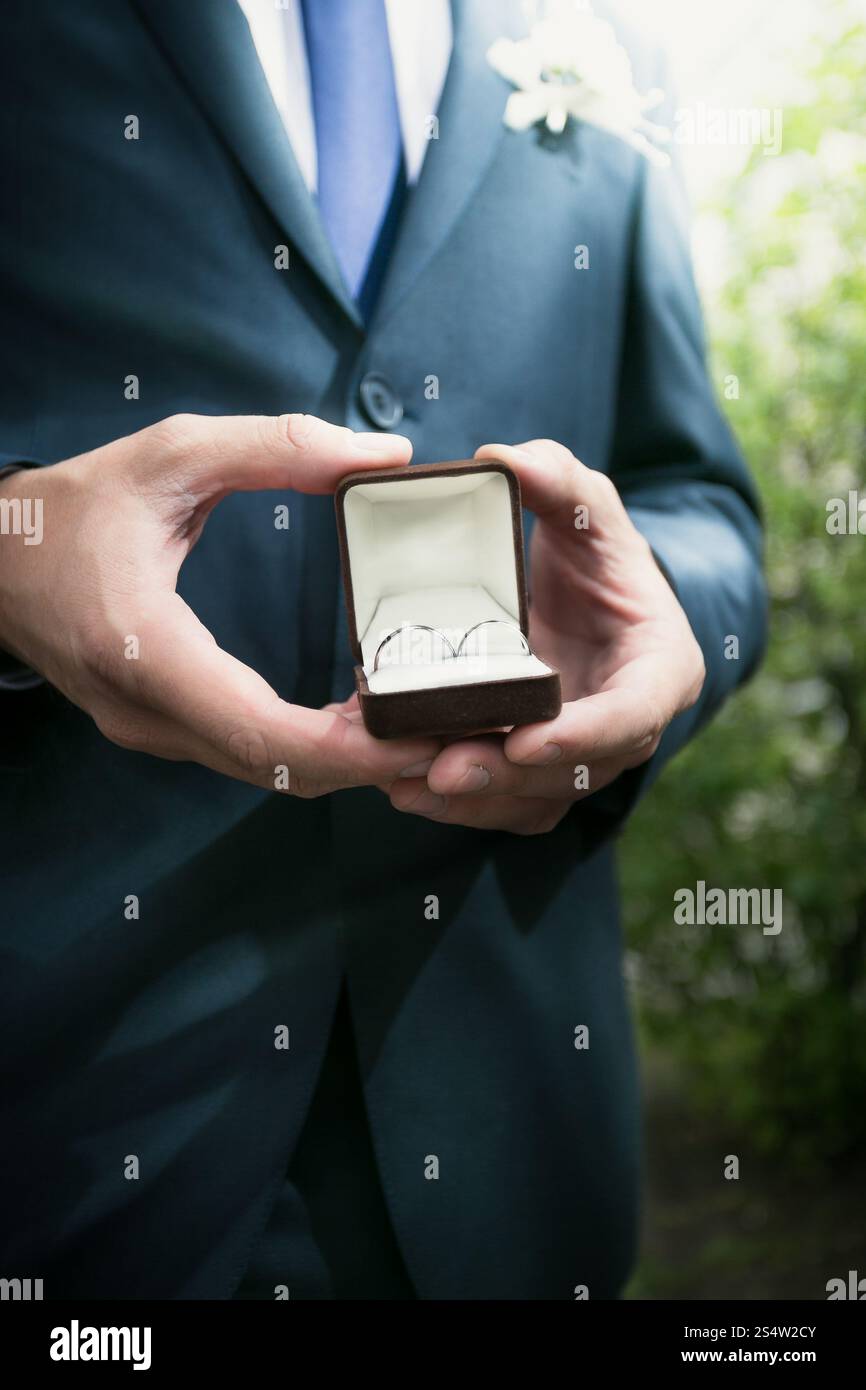 Nahansicht eleganter Bräutigam, der eine offene Box mit Eheringen hält Stockfoto