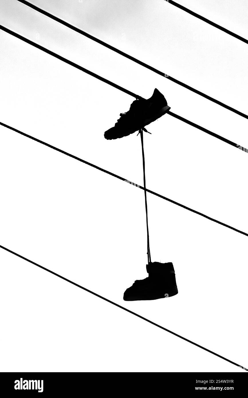 Ein Paar Sportschuhe hängt an den Schnürsenkeln an elektrischen Drähten. Stockfoto