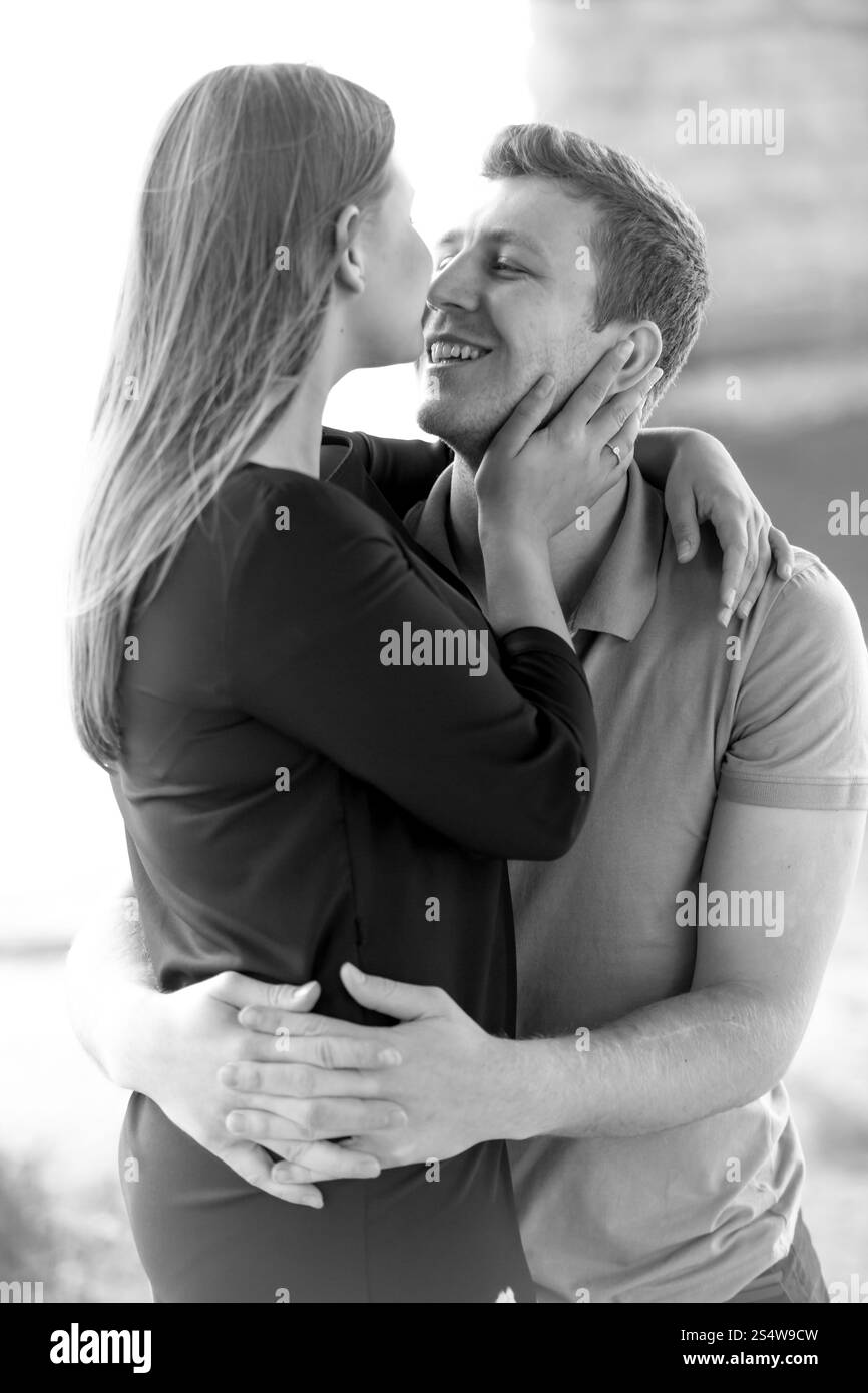 Schwarz-weiß-Porträt eines glücklichen Liebespaares, das sich am Fluss unter der Brücke küsst Stockfoto