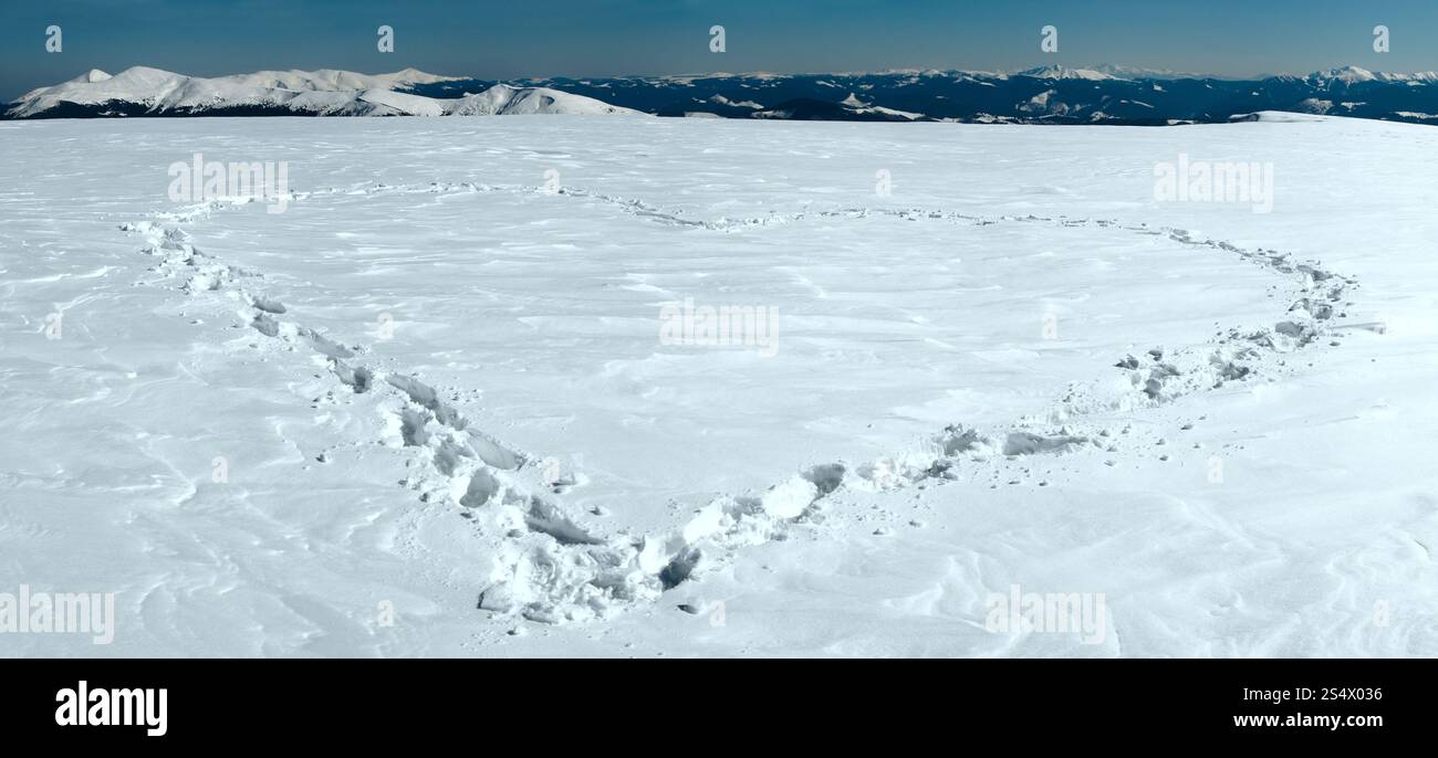 Menschlichen Fußabdruck bilden die Herzform auf schneebedeckten Berg-Plateau und Bergketten hinter. Stockfoto