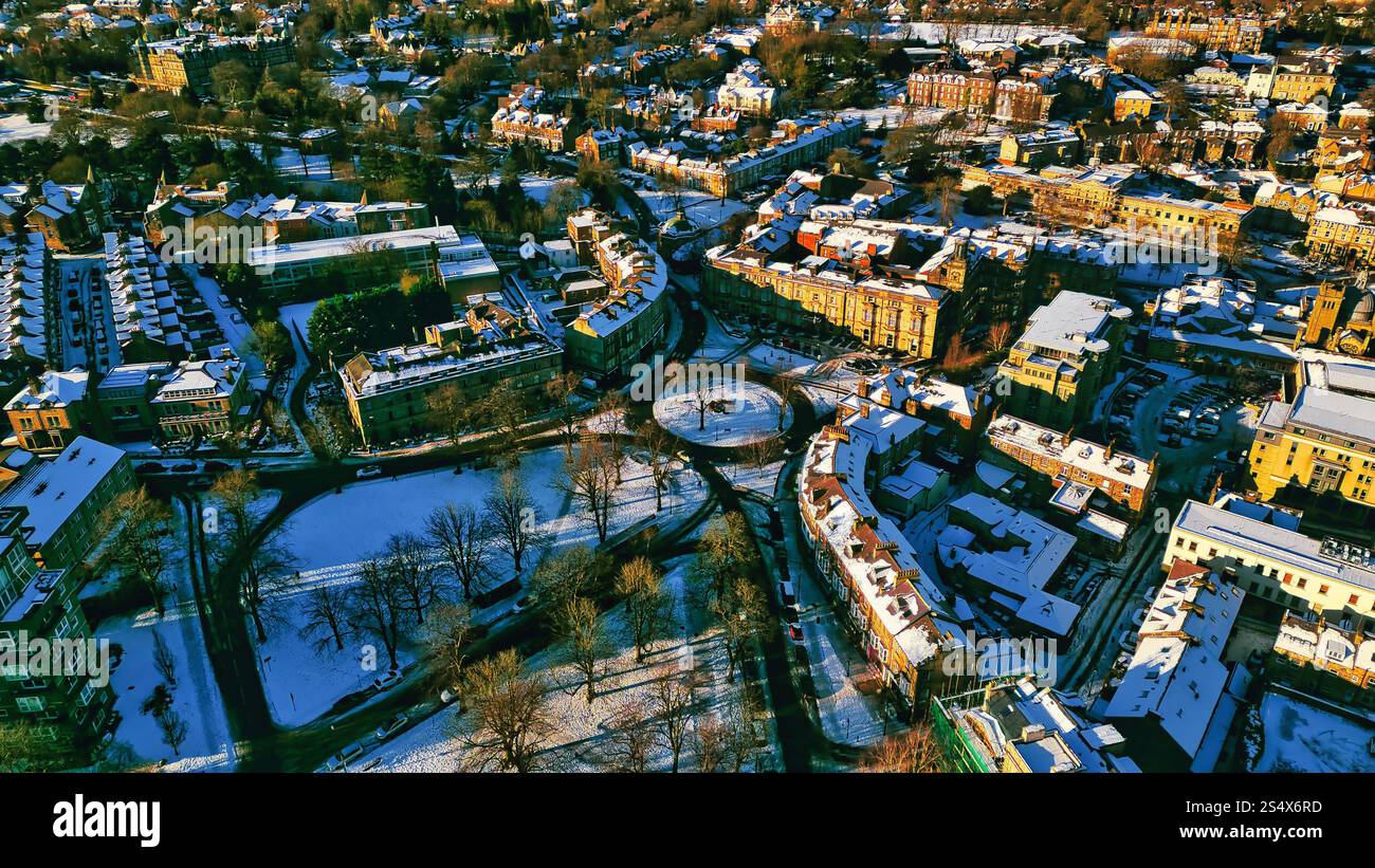 Aus der Vogelperspektive auf eine schneebedeckte Stadt mit Wohngebäuden, einem zentralen Park und Straßen. Die Gebäude sind hauptsächlich mehrstöckig und mit geneigtem Dach Stockfoto