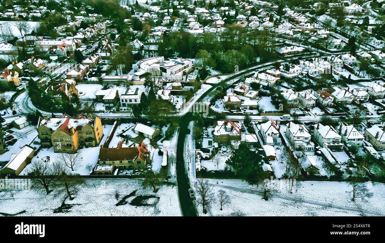 Aus der Vogelperspektive auf ein schneebedecktes Wohngebiet mit verschiedenen Häuserstilen, Straßen und Grünflächen. Ein großes Gebäude ist zentral gelegen. Die V Stockfoto